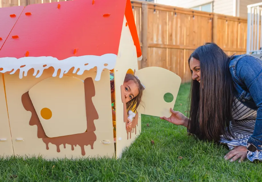 A mother playing peekaboo with her child through a red-roof NimoPlay house door
