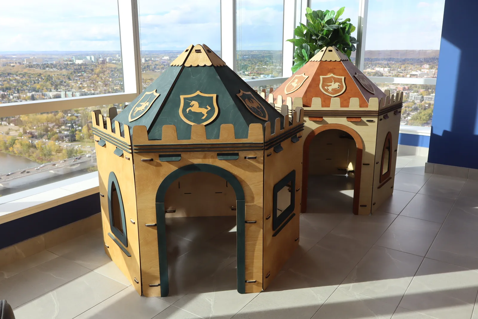Green and brown NimoPlay castle playhouses standing side by side in a sunny room